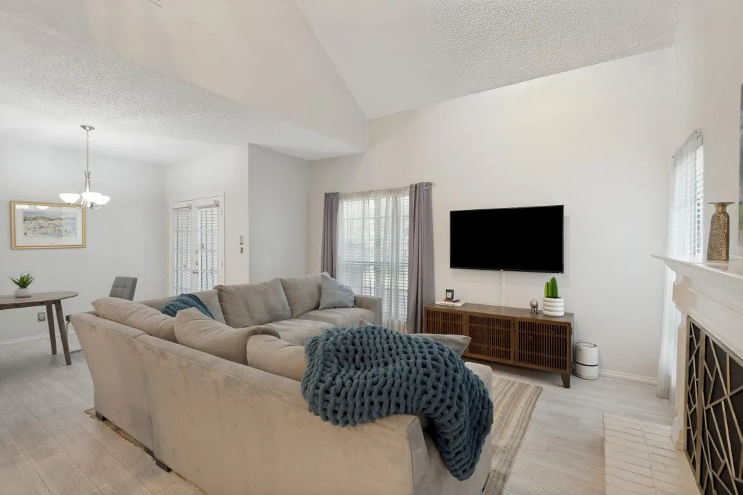 Vaulted ceiling living area with light-toned wood-finish flooring, a white-painted fireplace mantel, and recessed window