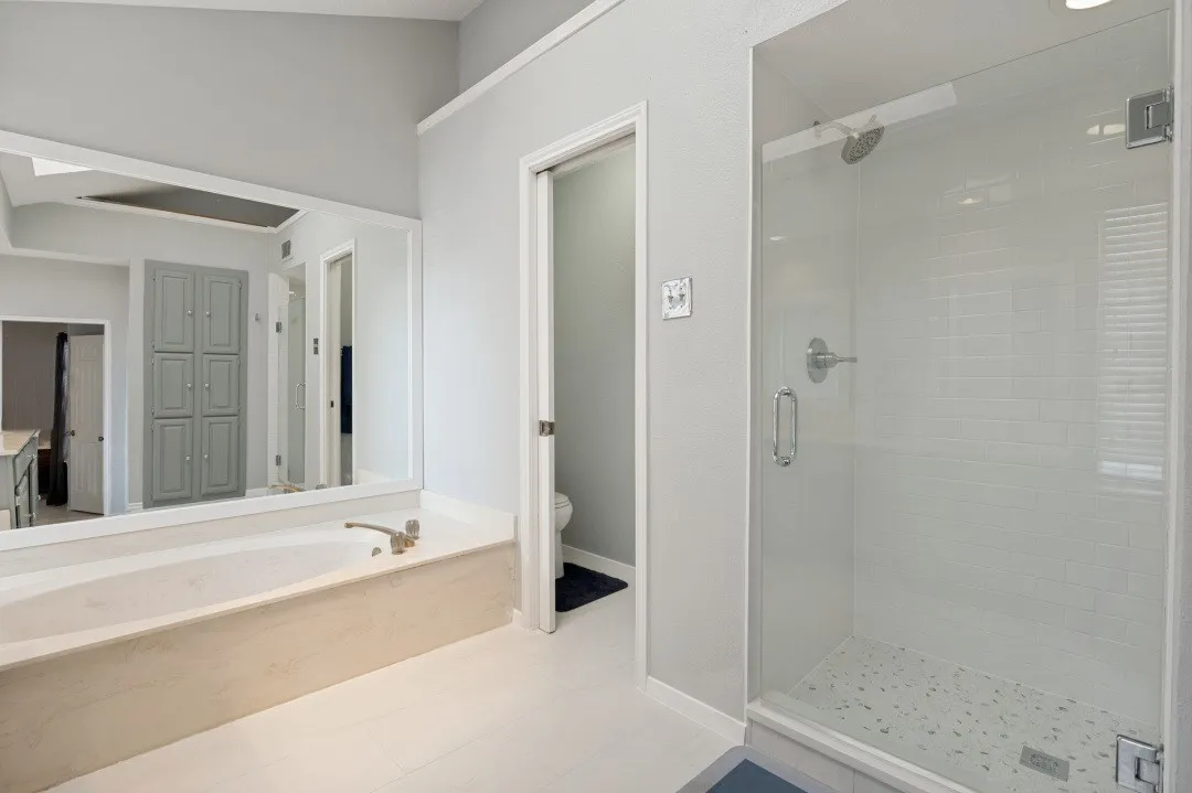 Soaking tub with a large wall-mounted mirror, glass-enclosed shower with subway tile surround, and vaulted ceilings