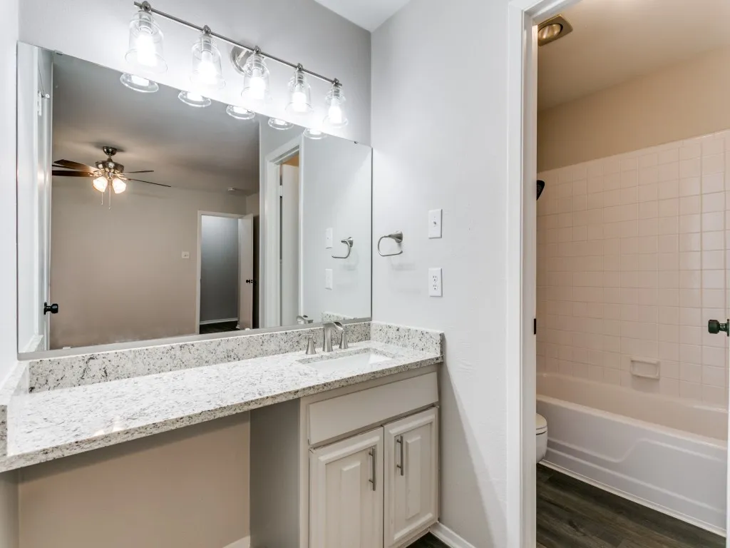 Bathroom vanity featuring a speckled countertop, a single undermount sink with a chrome faucet, and white shaker-style cabinetry with chrome pulls