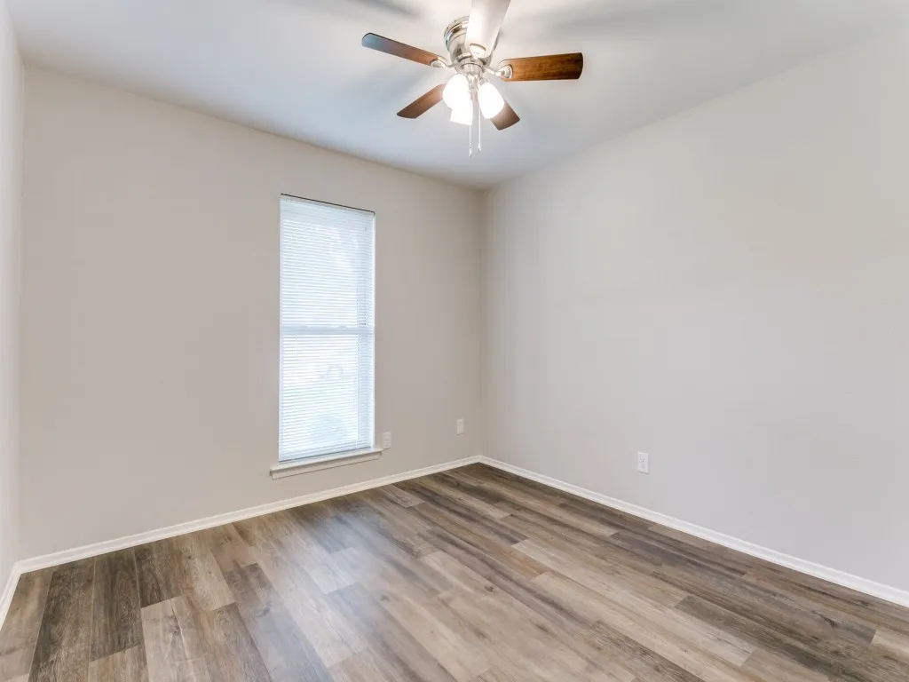 Room featuring wood-finish flooring, a single window with horizontal blinds, and a ceiling fan with light fixture