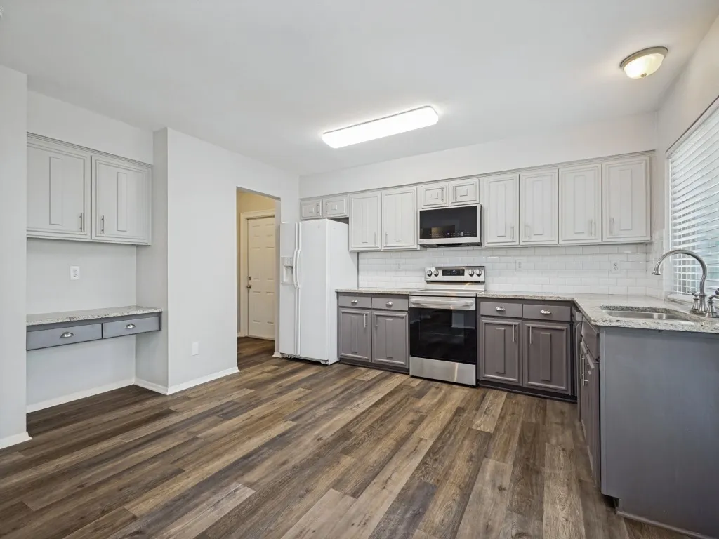 Open-concept kitchen featuring wood-finish flooring, two-tone cabinetry, stainless steel appliances, speckled countertops, and a subway tile backsplash