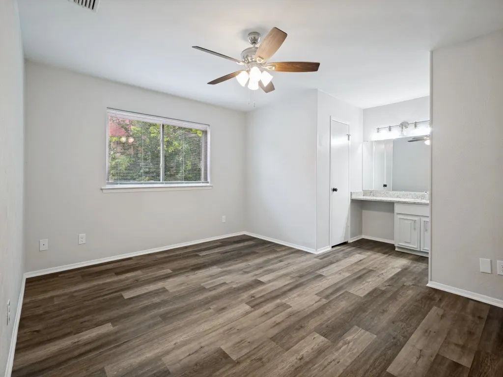 Spacious room featuring wood-finish flooring, a ceiling fan with light fixture, and a large window