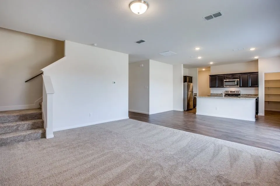 Open-concept living area featuring a kitchen with dark wood-finish cabinetry, stainless steel appliances, and a breakfast bar with a light-toned countertop