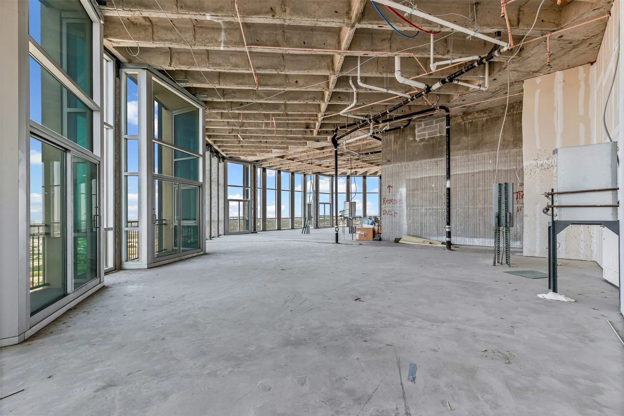 Expansive open-concept space featuring a concrete slab floor, exposed ceiling with visible utilities, and a curved wall of floor-to-ceiling windows