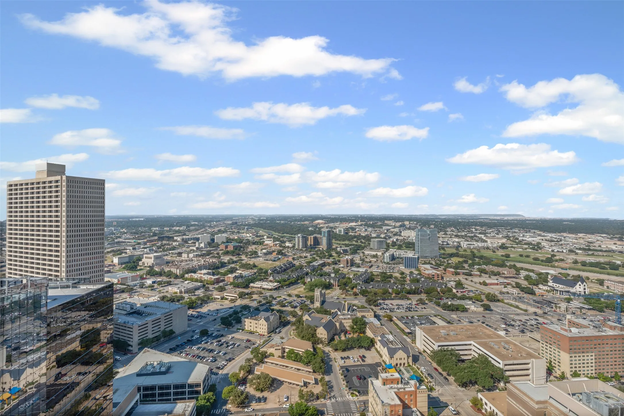 Expansive cityscape featuring a variety of urban structures, distant green spaces, and a clear sky with scattered clouds