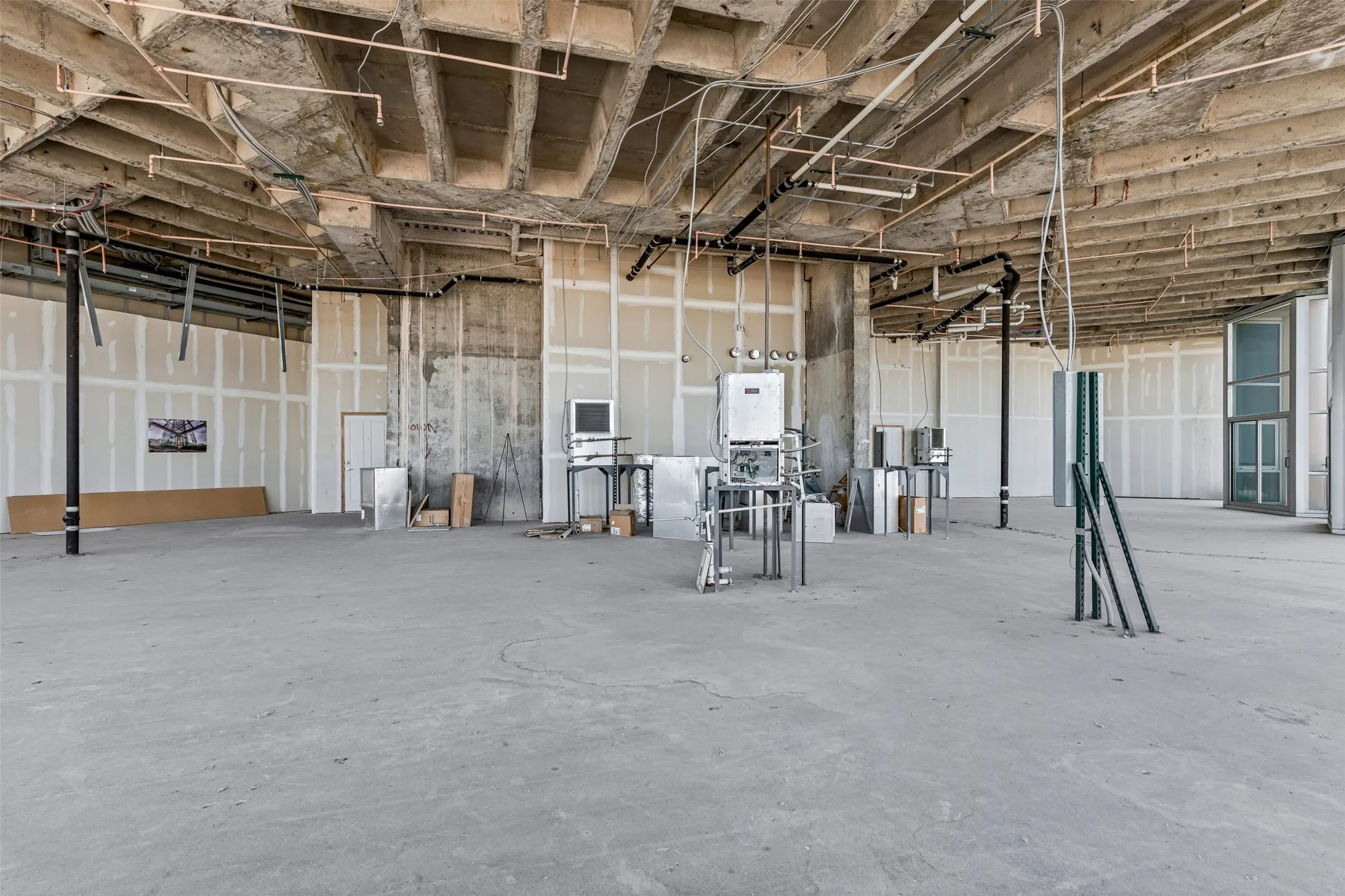 Spacious interior featuring exposed concrete ceilings with visible utility infrastructure, unfinished drywall partitions, and a concrete floor
