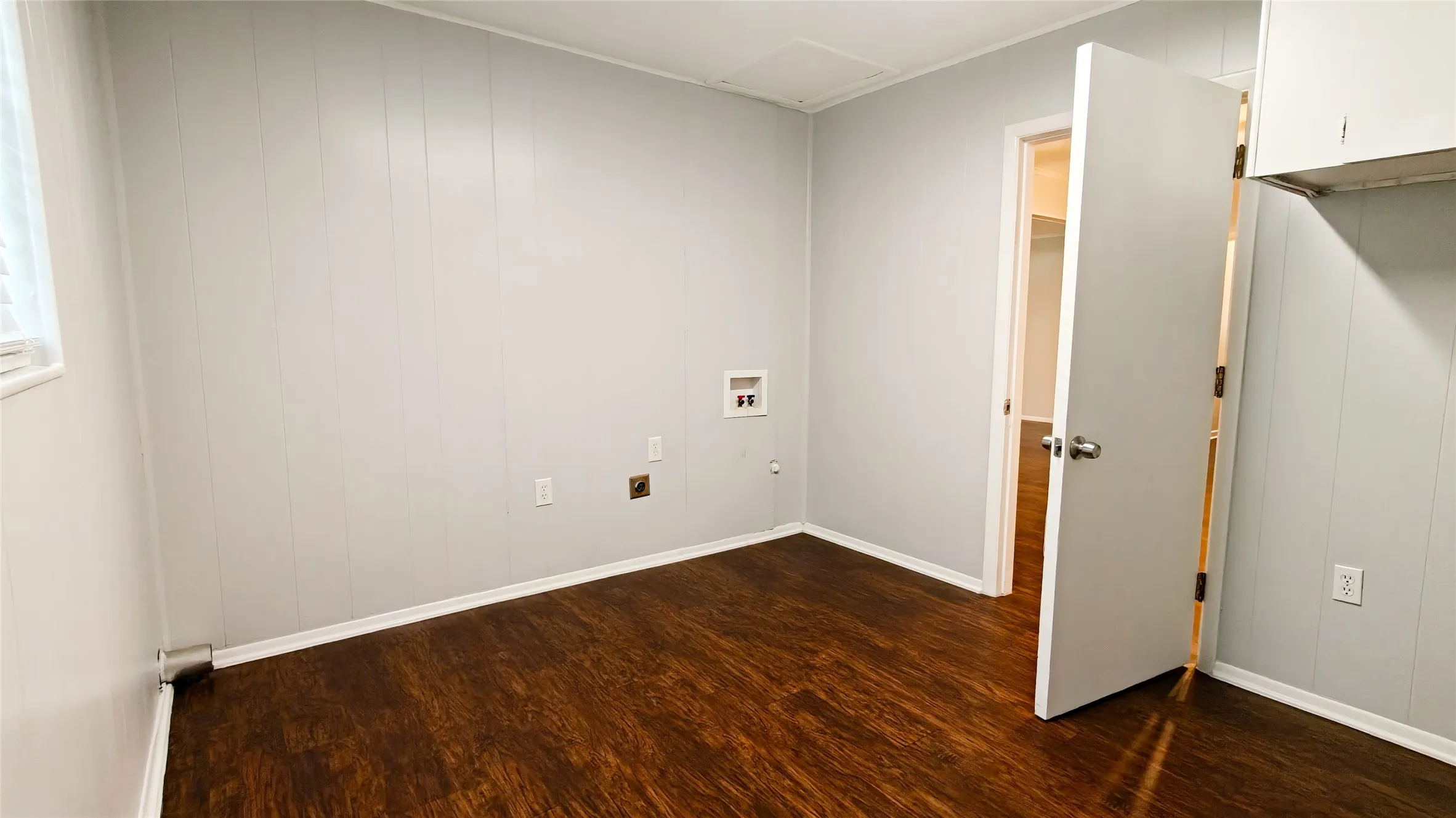 Dedicated utility area featuring wood-finish flooring, light grey paneled walls, and white baseboards