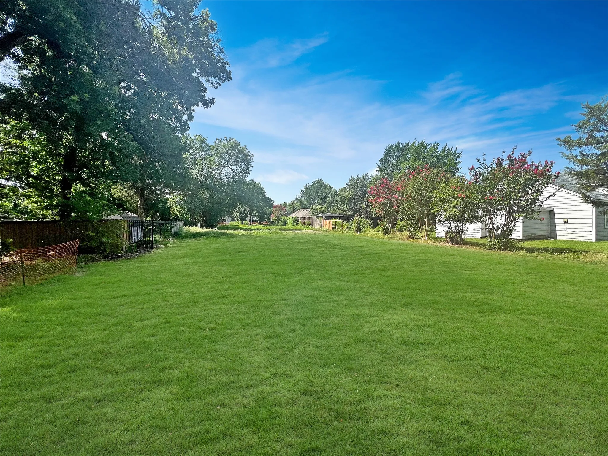 Expansive grassy lot with established trees and partial fencing
