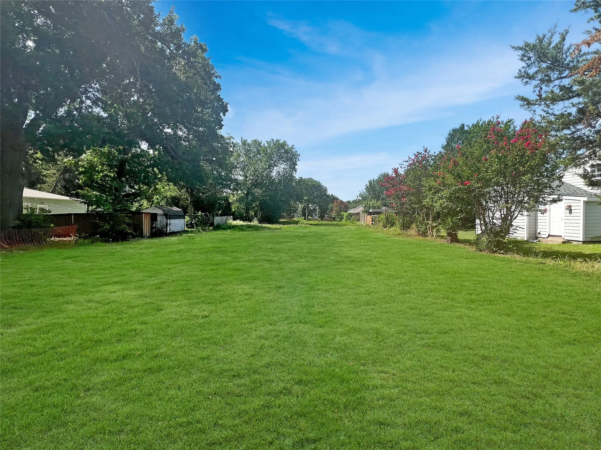 Expansive green lawn with mature perimeter trees and flowering bushes