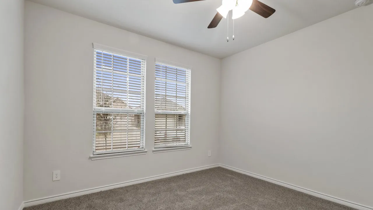 Bright interior room featuring two windows with horizontal blinds, neutral-toned walls, and a ceiling fan with integrated lighting