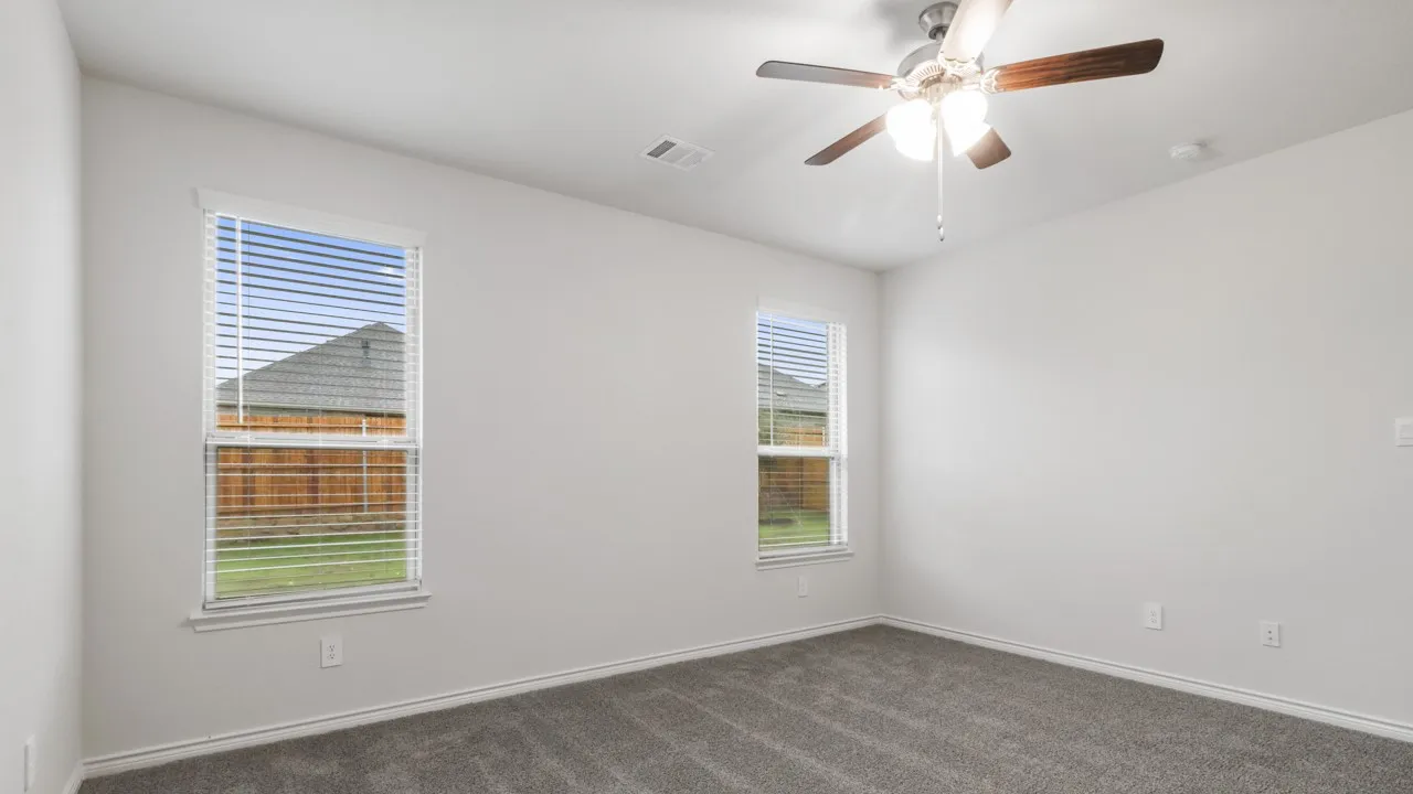 Carpeted interior room featuring two windows with blinds, a ceiling fan with light fixture, and light-colored walls