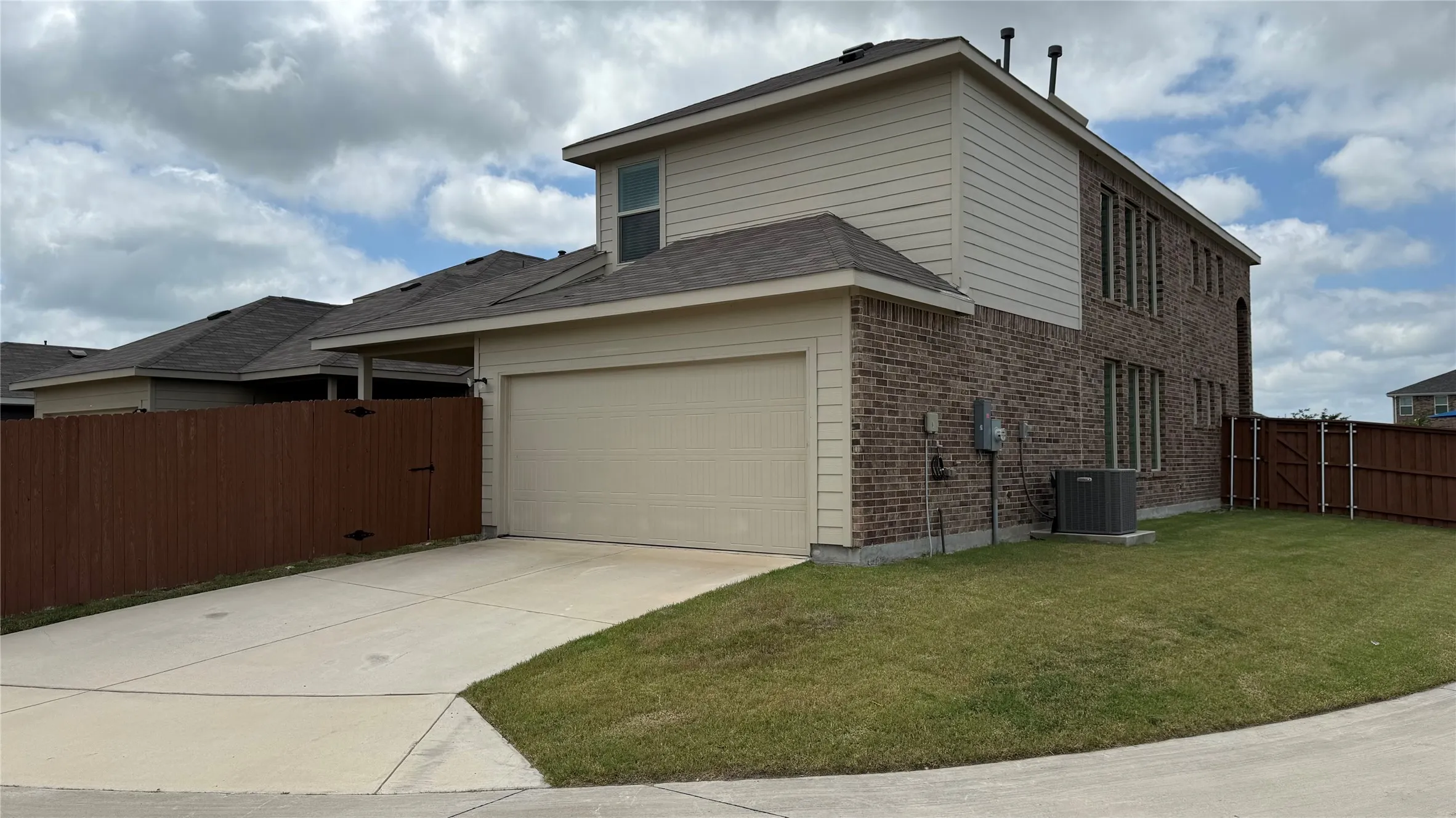 Two-story residence featuring a two-car garage, brick and siding exterior, and a privacy fence enclosing the yard