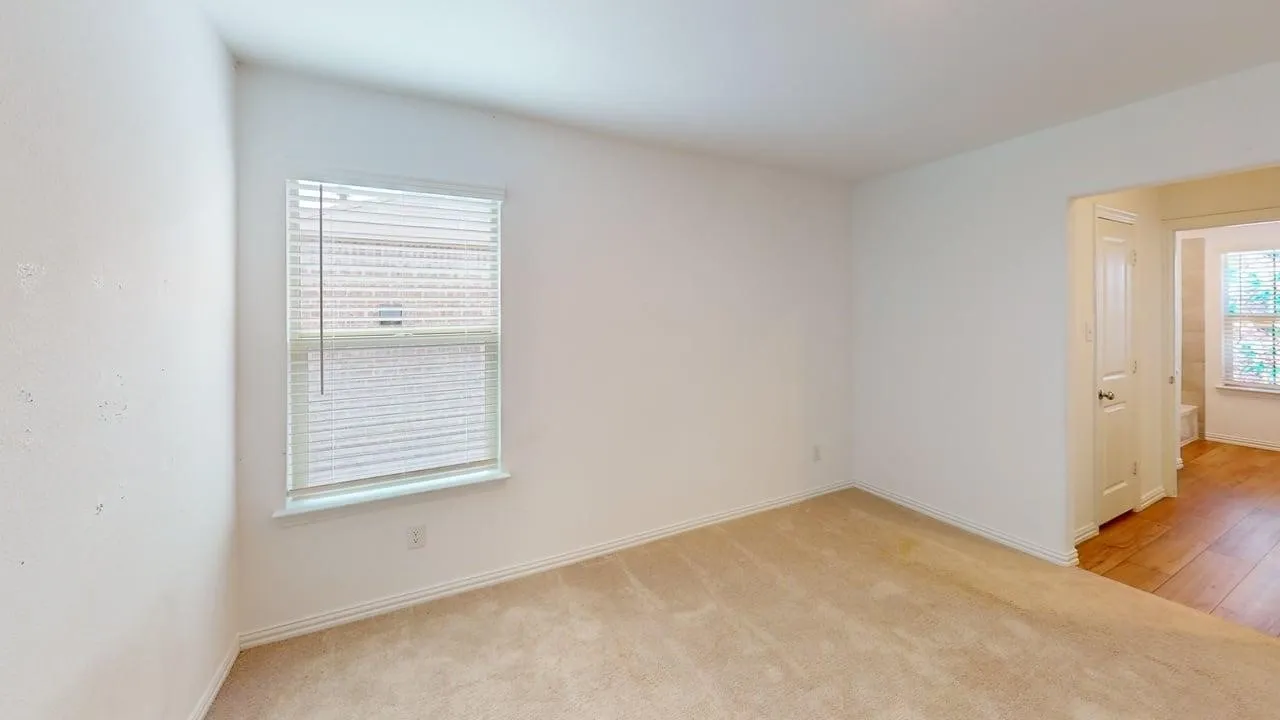 Neutral carpeted room with a single window featuring horizontal blinds