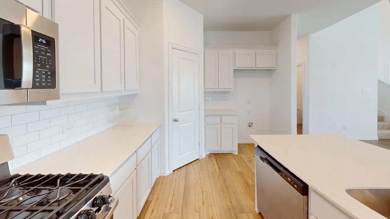 Bright kitchen featuring white cabinetry, subway tile backsplash, stainless steel appliances, extensive countertop space, and wood-finish flooring