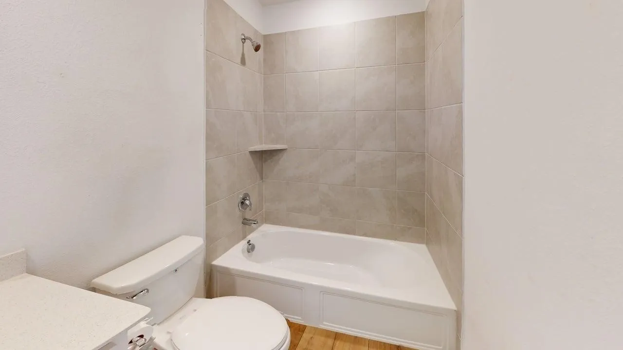 Bathroom featuring a white bathtub with a tiled shower surround, integrated shelf, and chrome fixtures