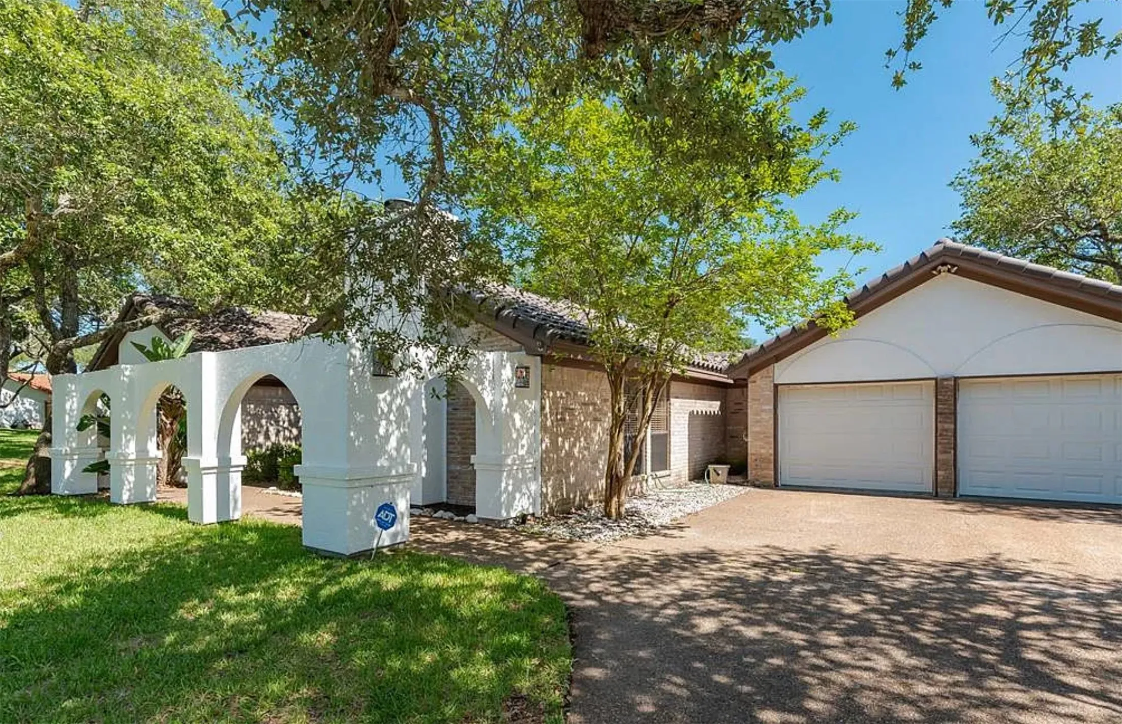 Mediterranean-style exterior featuring a white stucco facade with architectural archways, a two-car garage with white doors, and a tiled roof