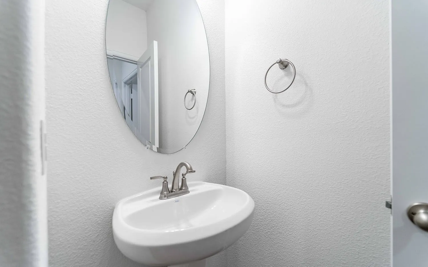 White pedestal sink with brushed nickel faucet, complemented by an oval wall-mounted mirror