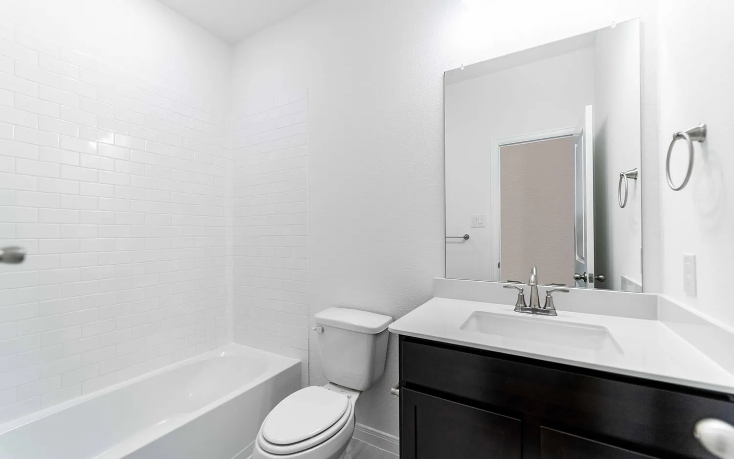 Bathroom with white subway tile shower surround, dark wood-finish vanity, light countertop, and chrome fixtures