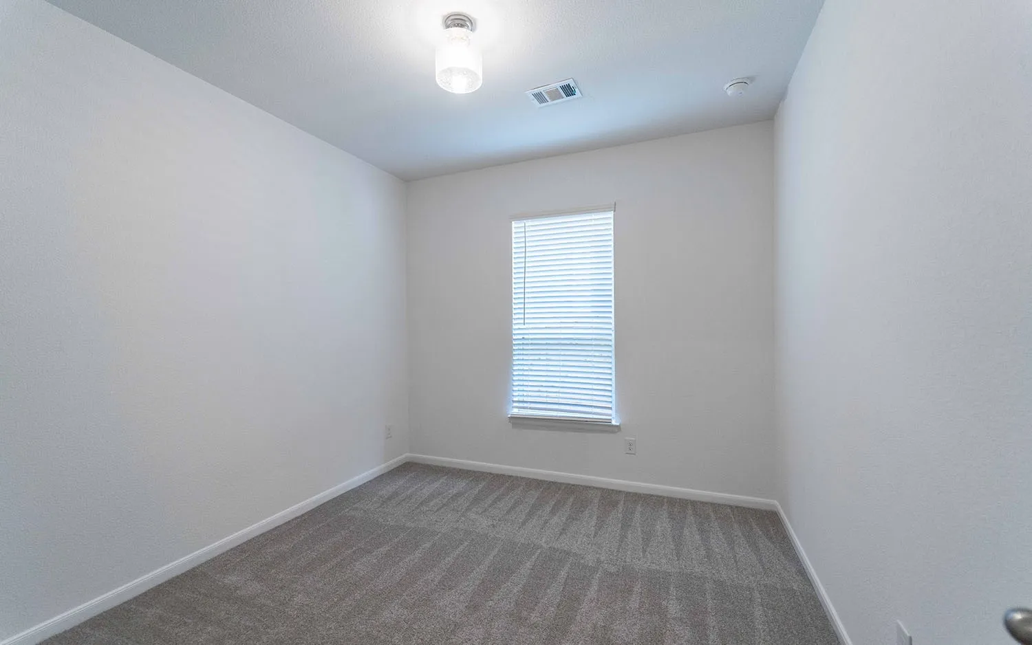 Room featuring light gray patterned carpeting, white painted walls, a single window with horizontal blinds, a white ceiling, and a ceiling-mounted light fixture