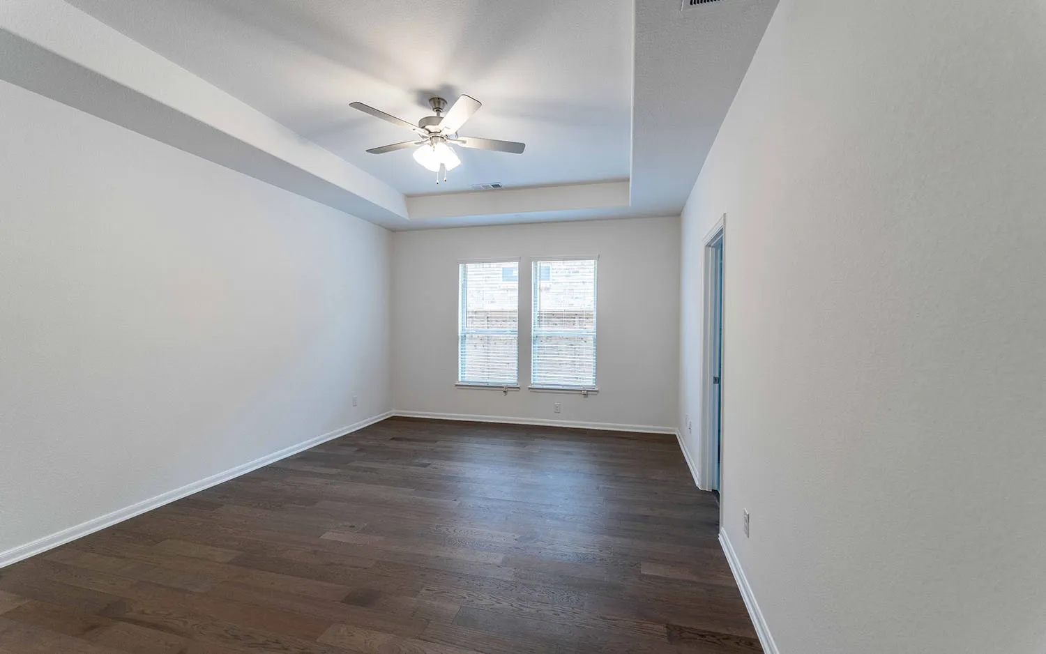 Spacious room featuring wood-finish flooring, a tray ceiling, and a ceiling fan