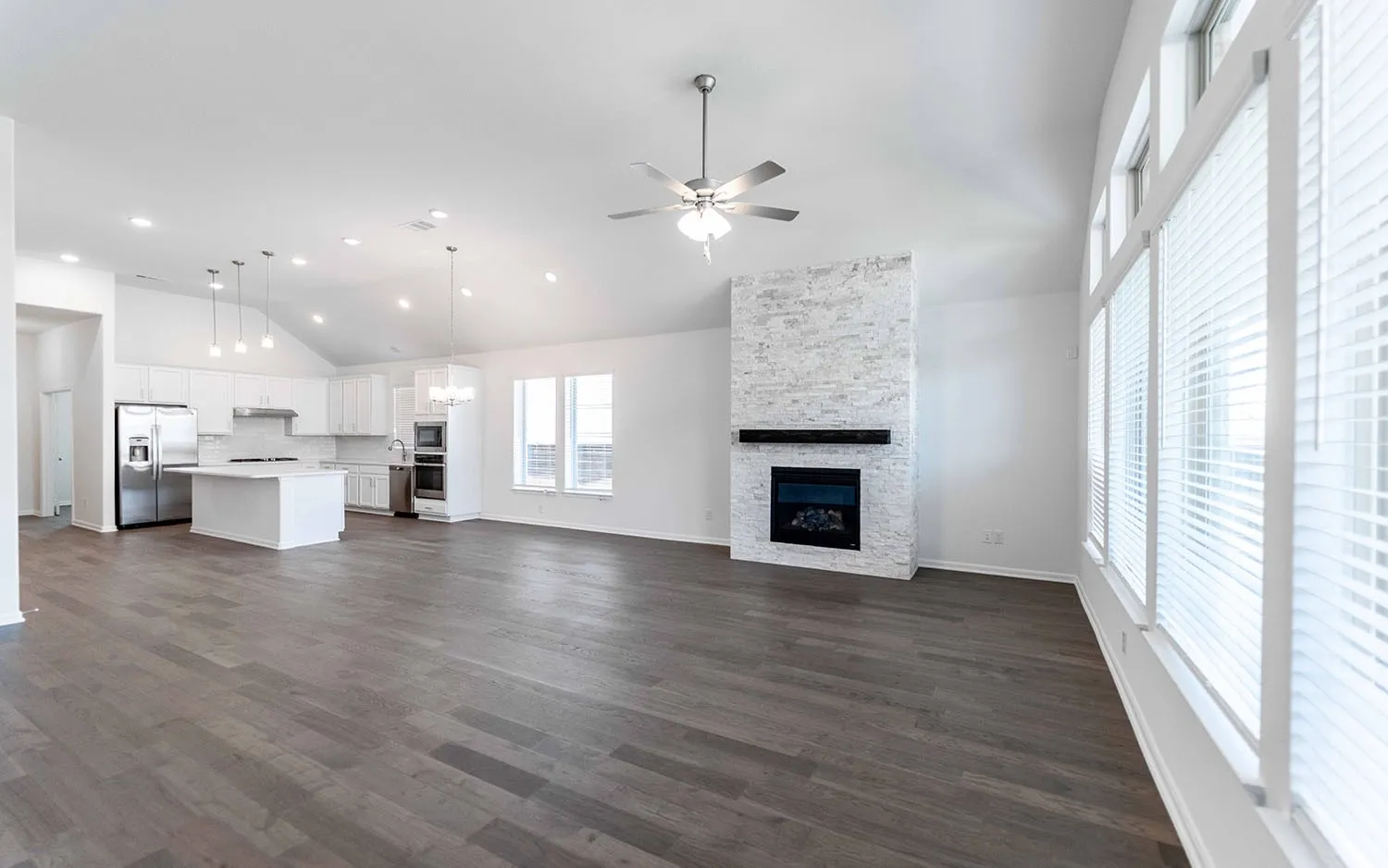 Expansive open-concept living space featuring vaulted ceilings, wood-finish flooring, and a stone-clad fireplace