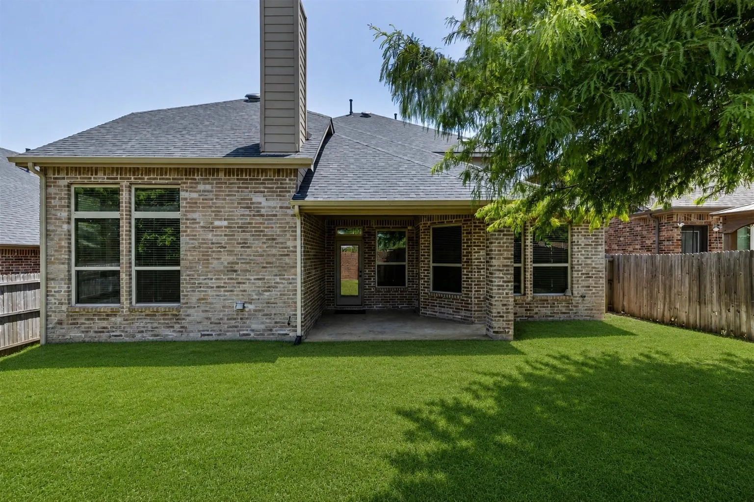 Expansive backyard with a covered patio, featuring a brick exterior and multiple windows