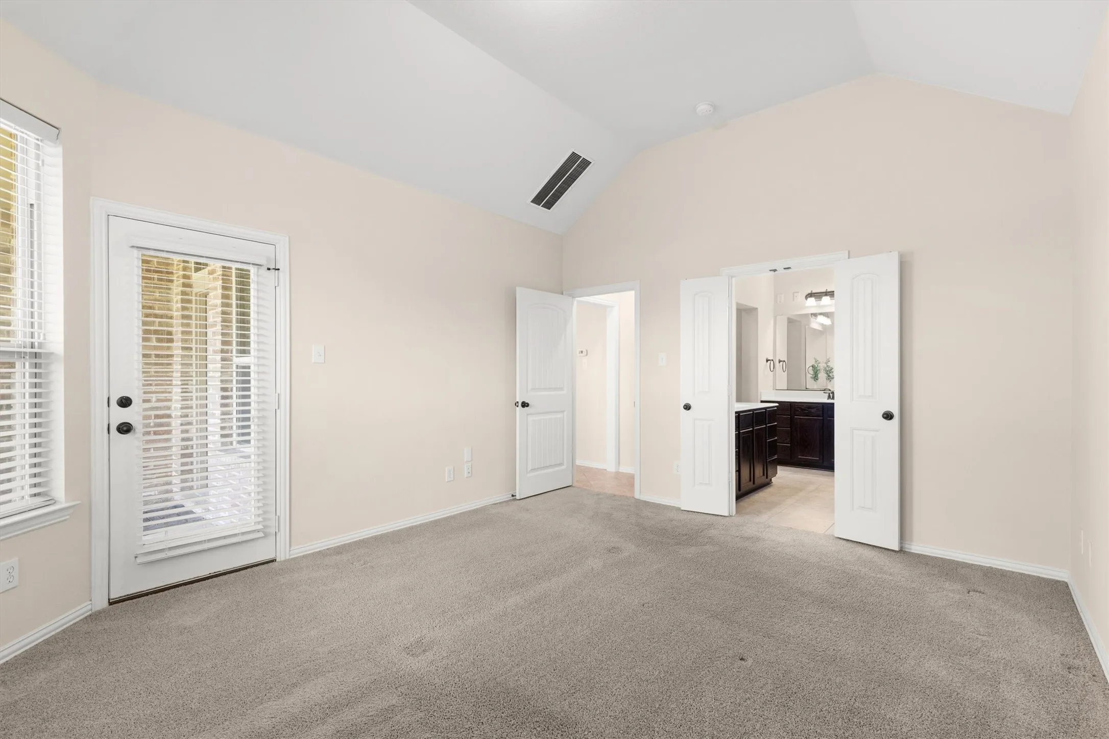 Vaulted ceiling room featuring carpet flooring, a glass-paned door, and a window with blinds