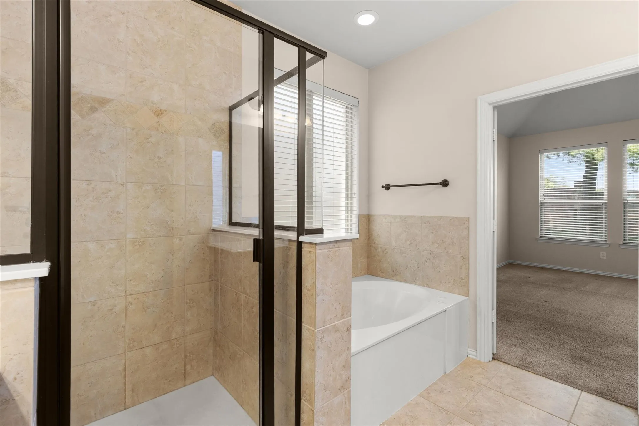 Walk-in shower with tiled walls and dark bronze-framed glass enclosure, deep soaking tub, and tiled flooring