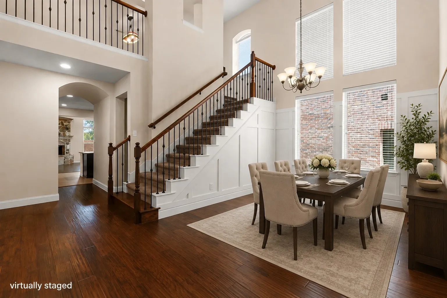 Soaring ceilings with upper windows, wood-finish flooring, a grand staircase with wrought iron balusters, and wainscoting detailing