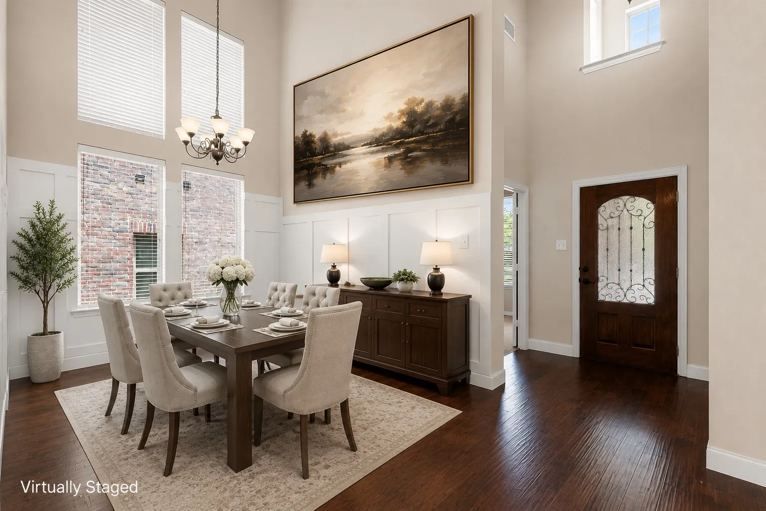 Two-story ceiling, dark wood-finish flooring, white paneling, wrought iron chandelier, and a decorative front door with an arched glass insert