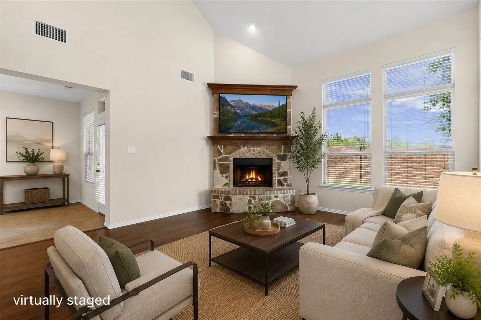 Vaulted ceiling living area featuring a stone-clad fireplace with wood mantel, wood-finish flooring, and multiple large windows