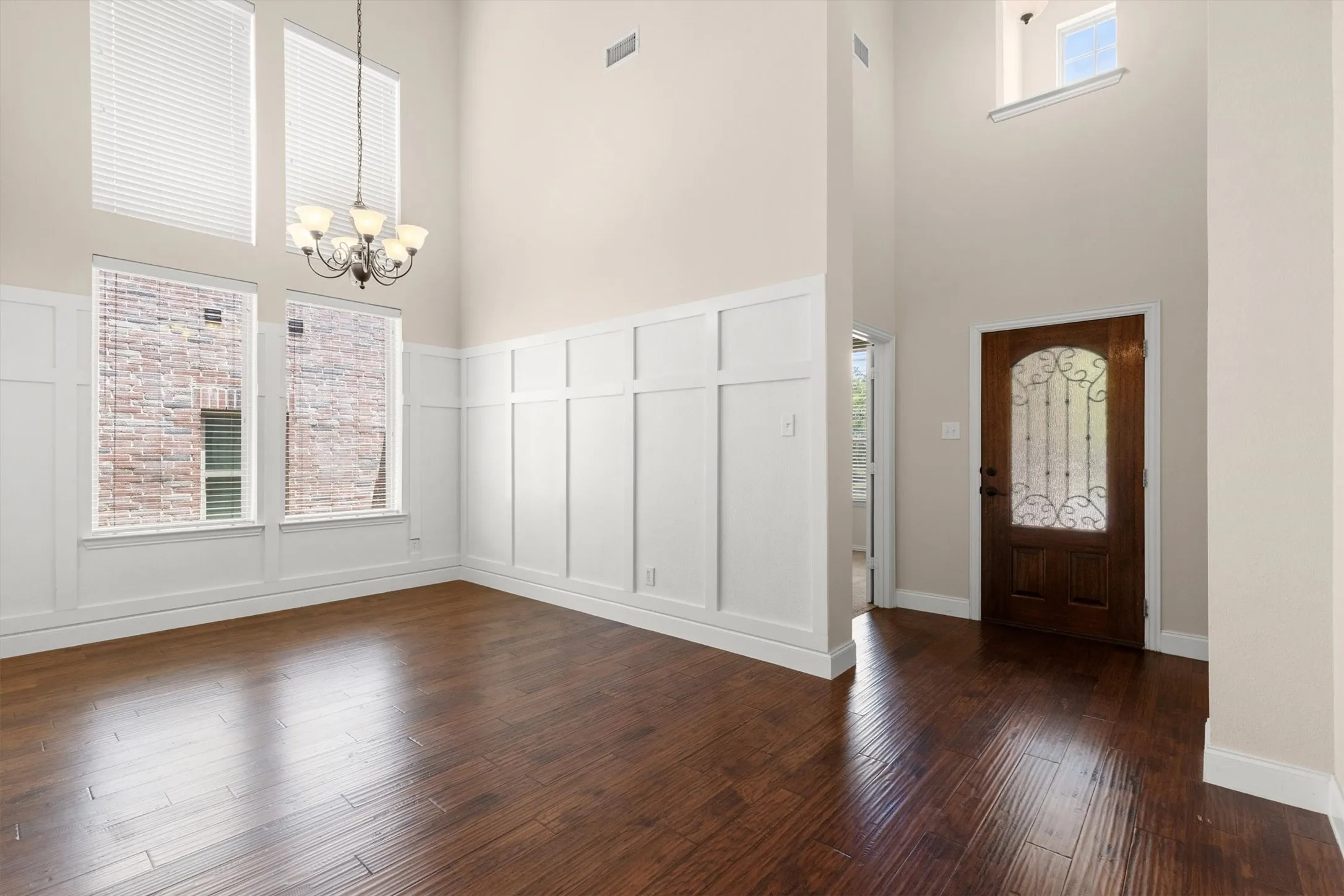Two-story entryway featuring a dark wood-finish front door with an arched glass insert, extensive wainscoting, and wood-finish flooring