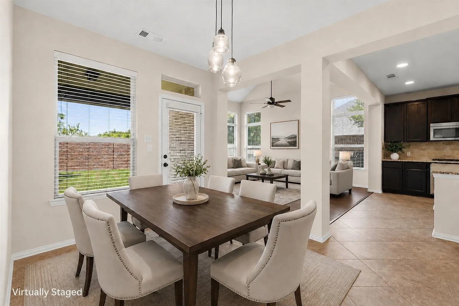 Open-concept layout with tile flooring, a kitchen featuring dark wood cabinetry and a microwave, a dining area with a multi-light pendant fixture, and a living area with a ceiling fan and large windows