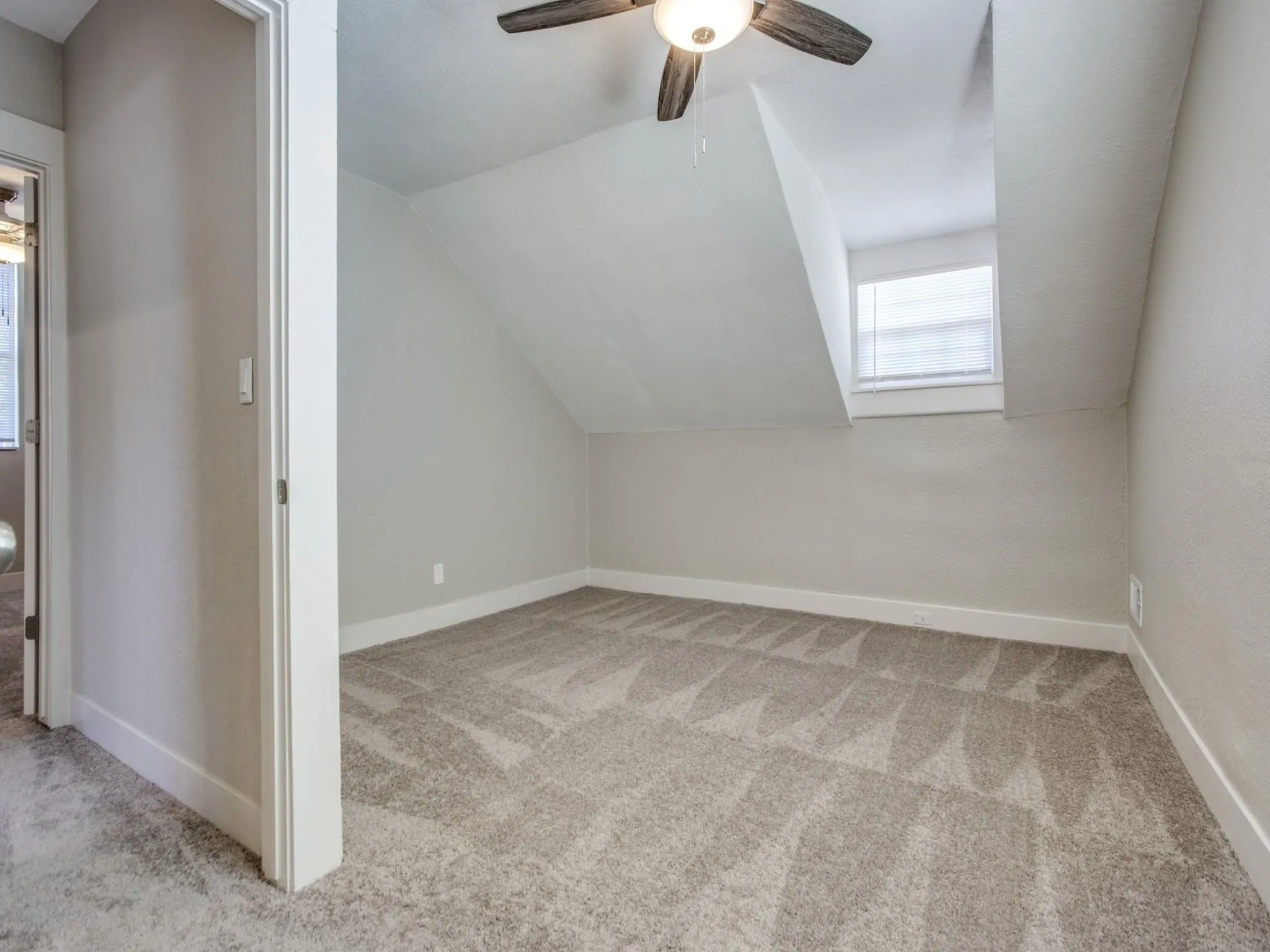 Carpeted room featuring a ceiling fan, sloped ceilings, and a window with blinds
