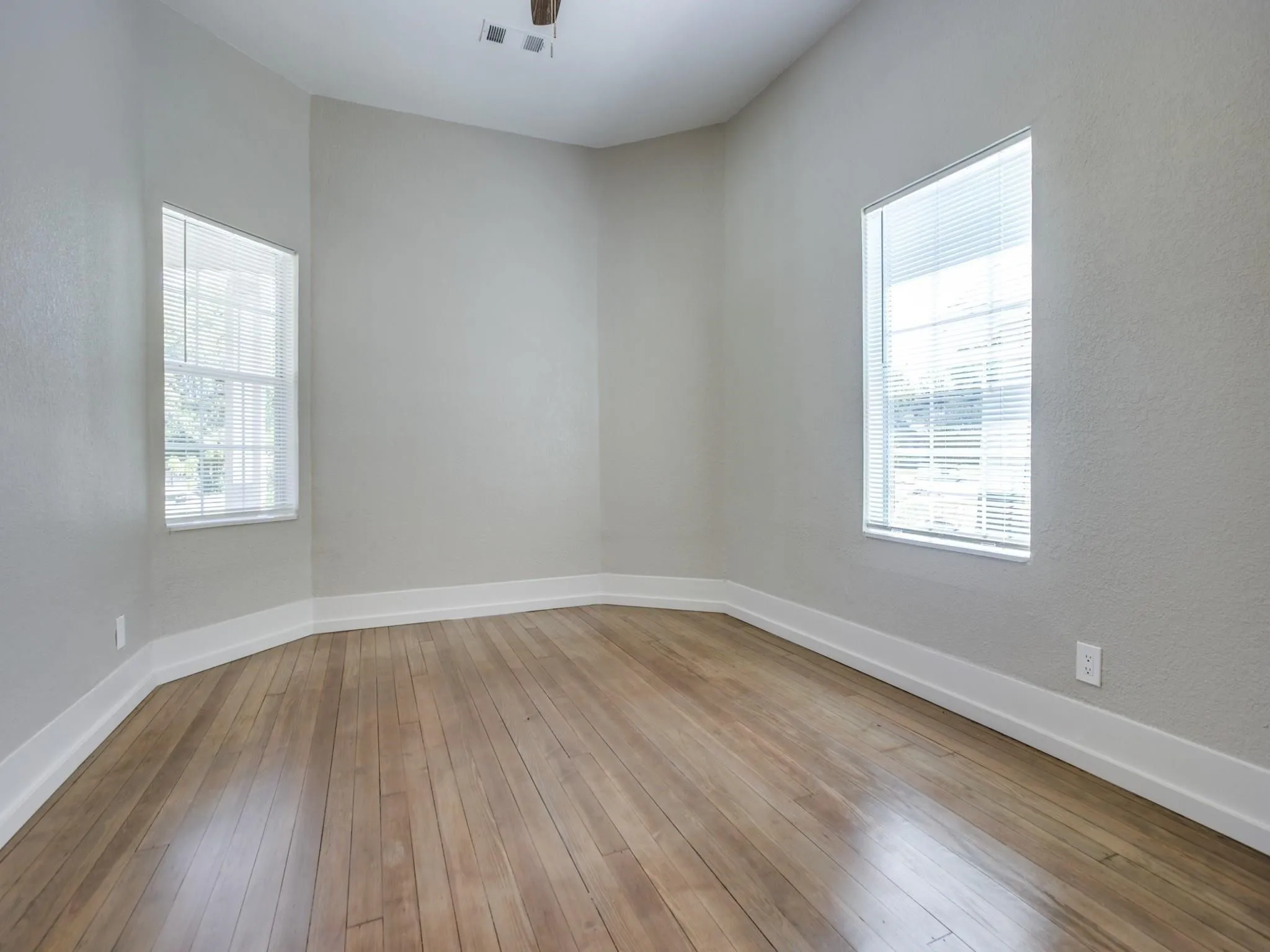 Bright room featuring wood-finish flooring, two windows with blinds, and light-toned wall paint