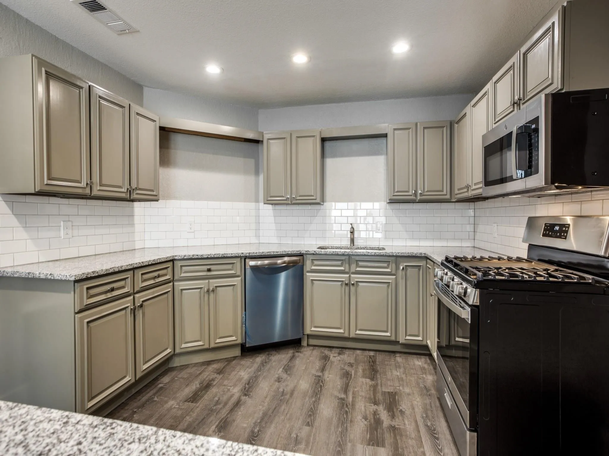Kitchen featuring extensive light-toned cabinetry, granite-finish countertops, subway tile backsplash, wood-finish flooring, and stainless-steel appliances
