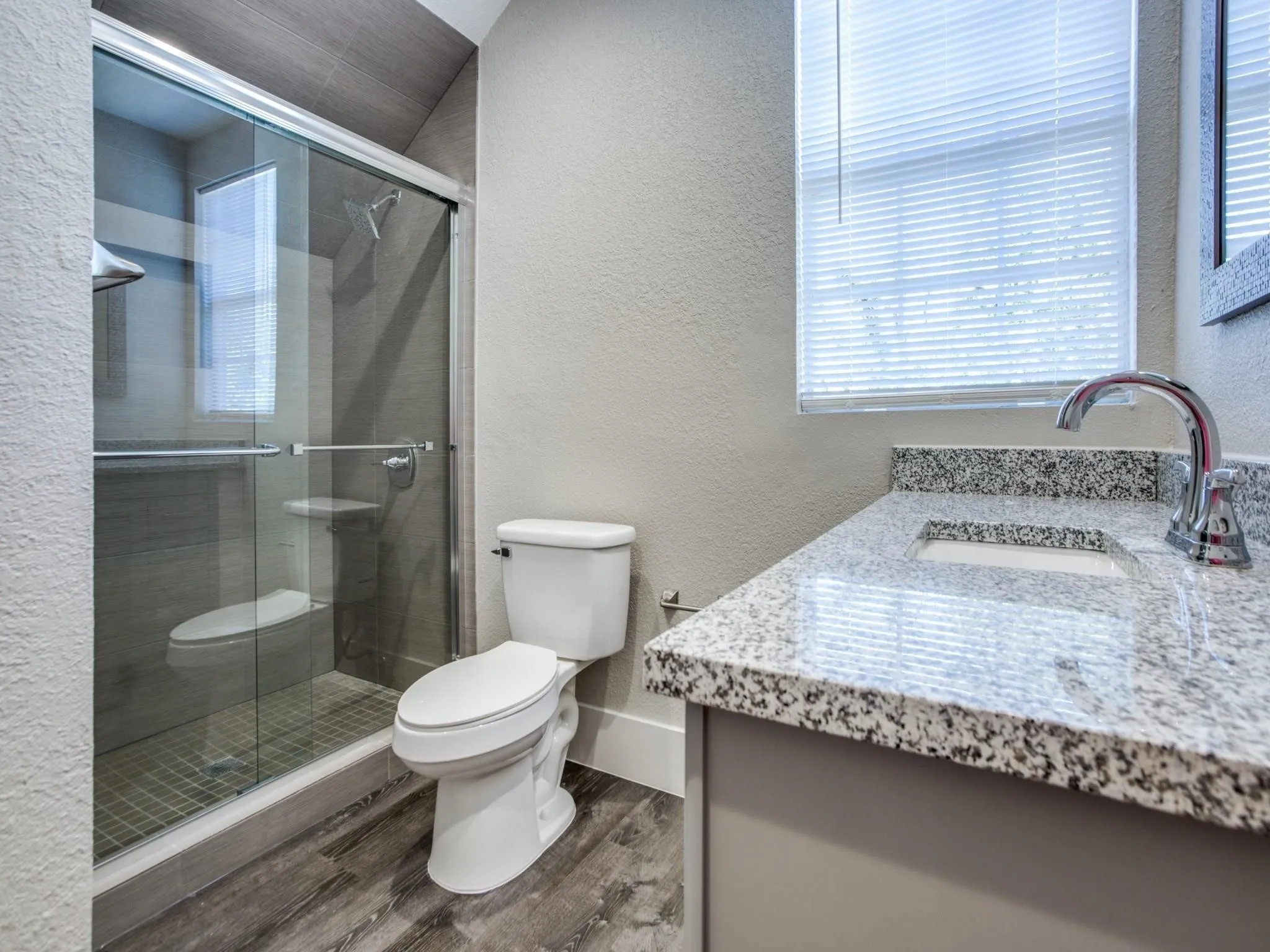 Bathroom featuring a glass-enclosed shower, stone-finish shower tiling, a vanity with a stone countertop, an integrated sink, and wood-finish flooring