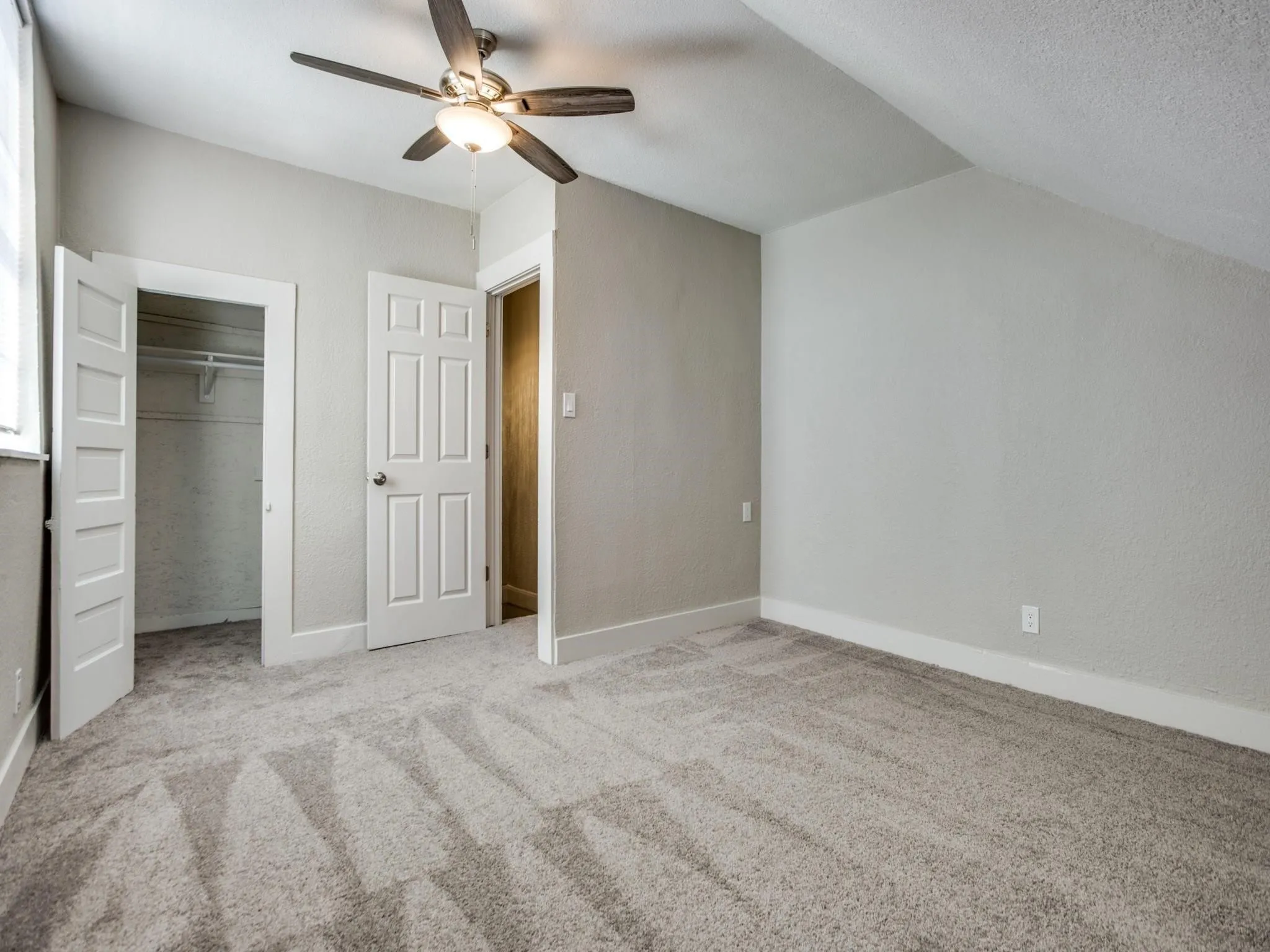 Spacious room featuring vaulted ceilings, a contemporary ceiling fan, plush carpet flooring, a closet with shelving, and a panel door