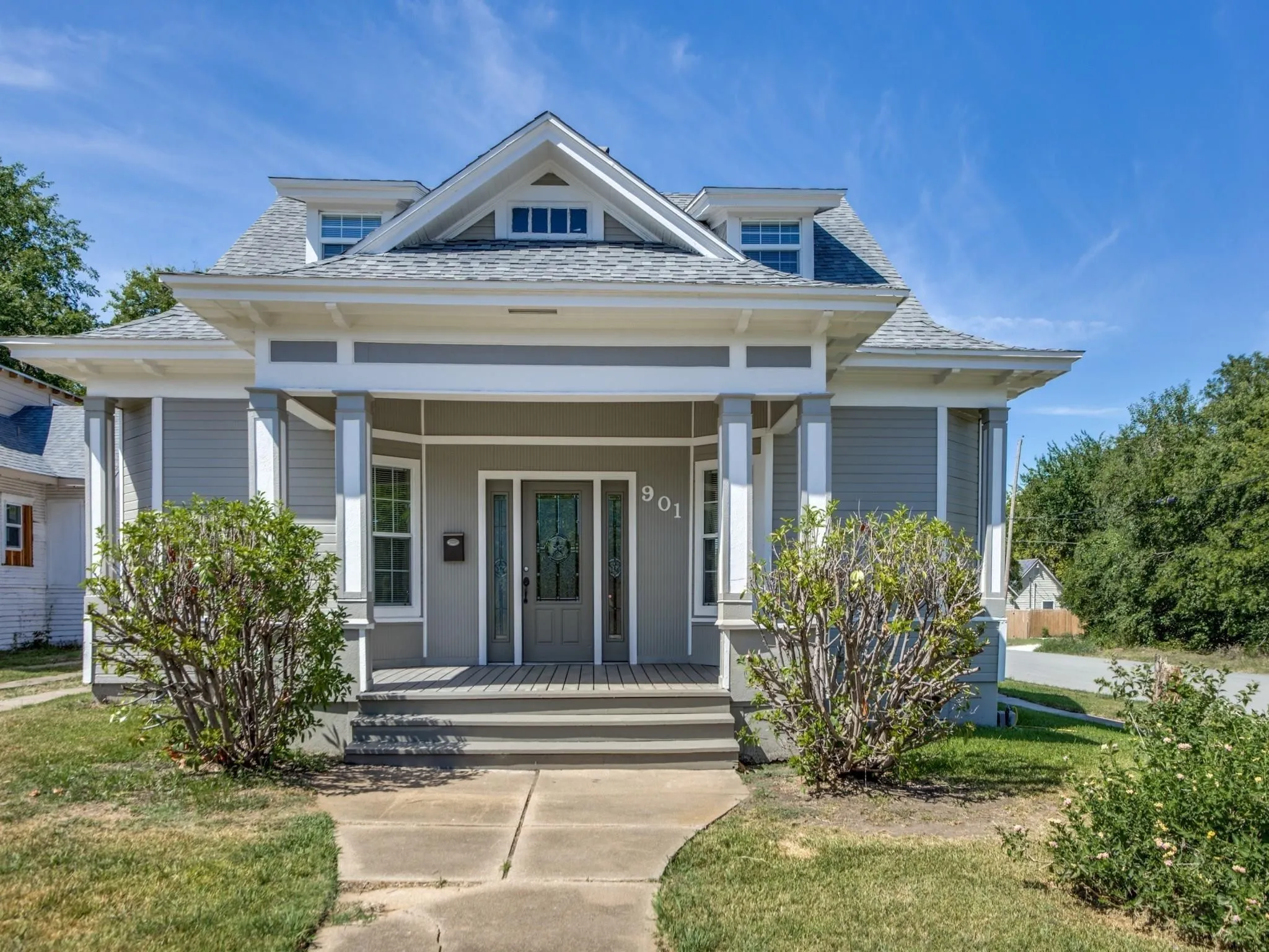 Gray siding exterior with white trim, featuring a covered front porch with square columns and a gabled roofline