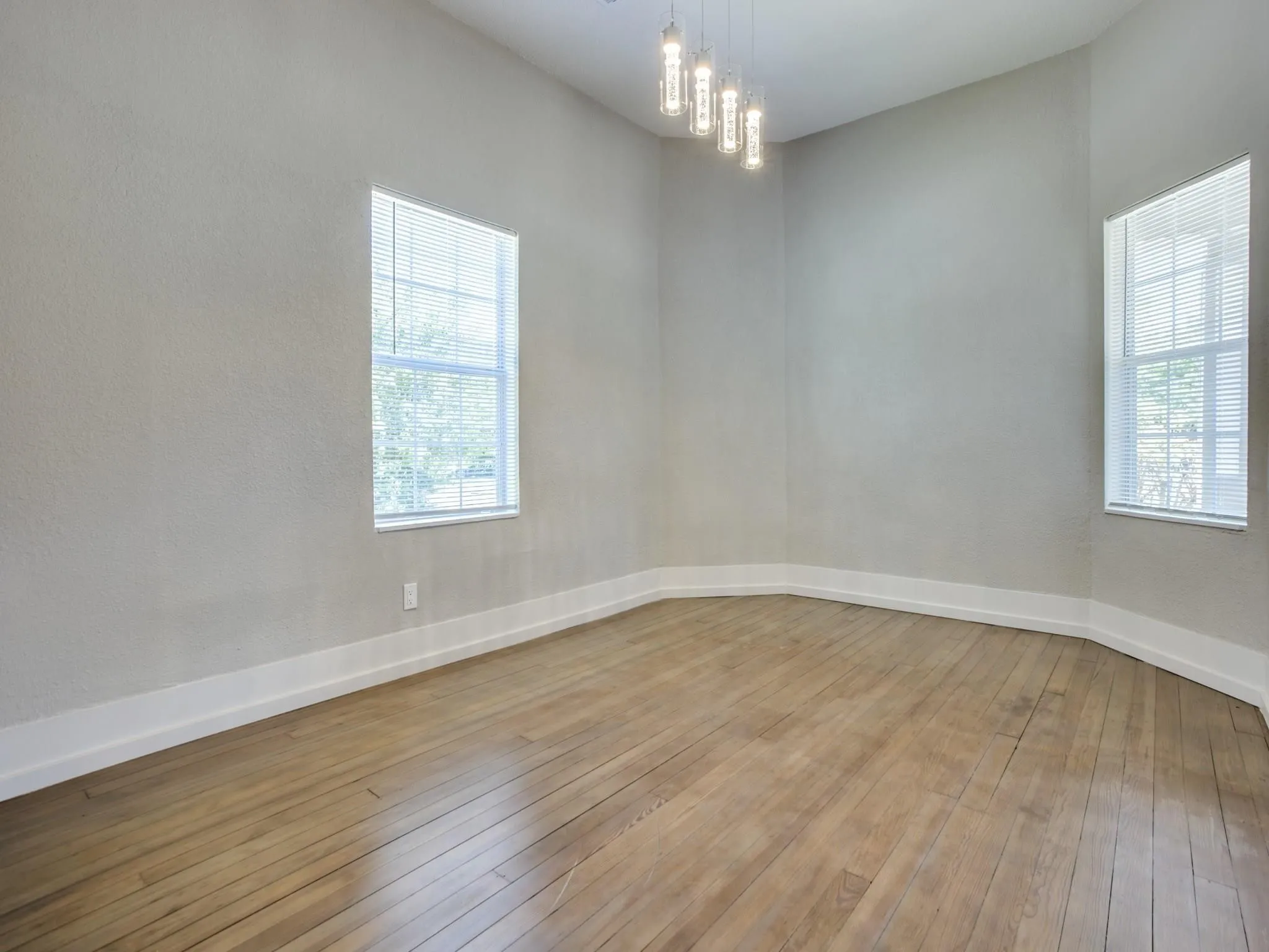 Spacious room featuring wood-finish flooring, high ceilings, and two large windows with blinds