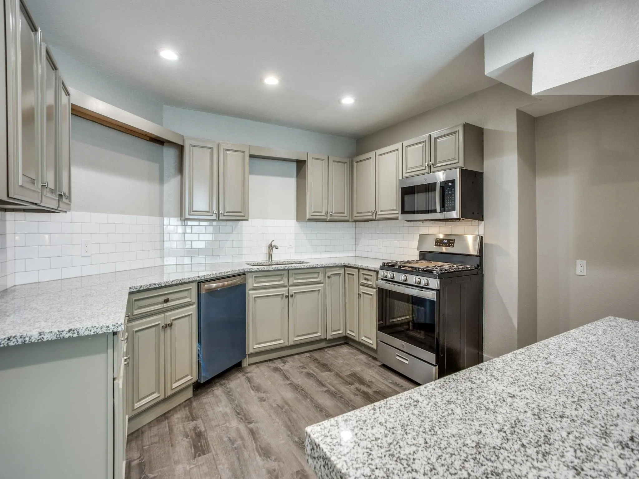 Kitchen featuring light-toned cabinetry, light-toned granite-style countertops, white subway tile backsplash, wood-finish flooring, and recessed lighting