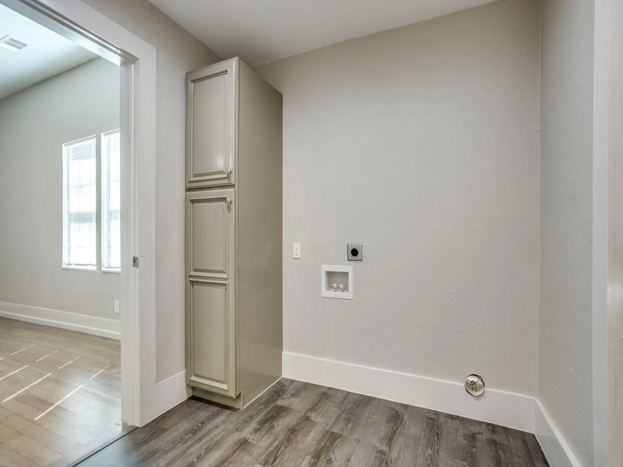 Laundry area featuring wood-finish flooring, light gray cabinetry, and white baseboards