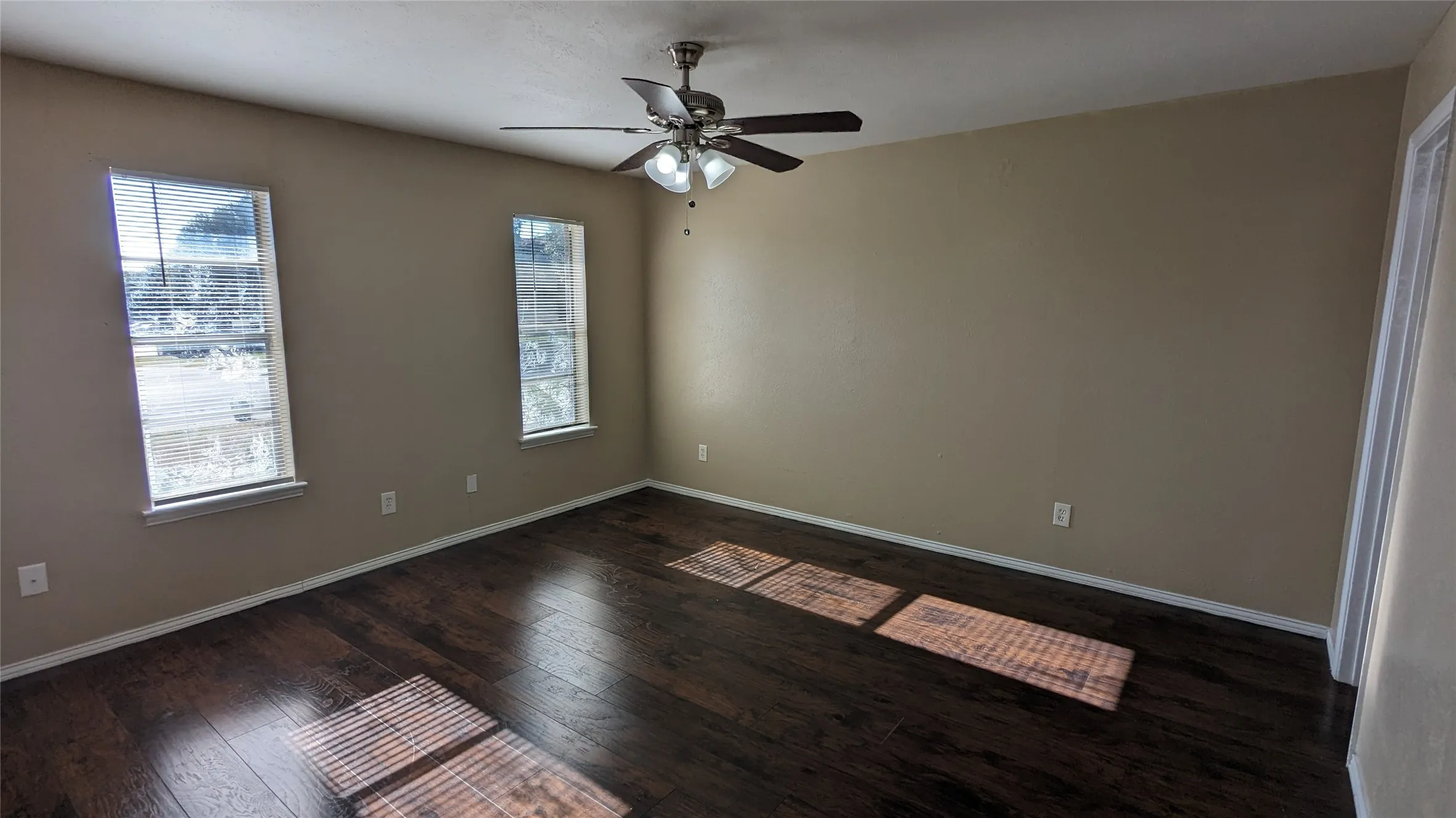 Spacious room featuring rich wood-finish flooring, neutral wall tones, and white trim