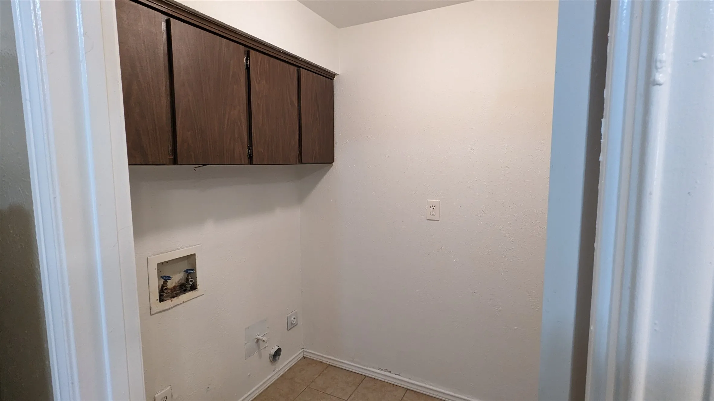 Laundry area with wood-finish upper cabinetry, a utility sink connection, and tile flooring