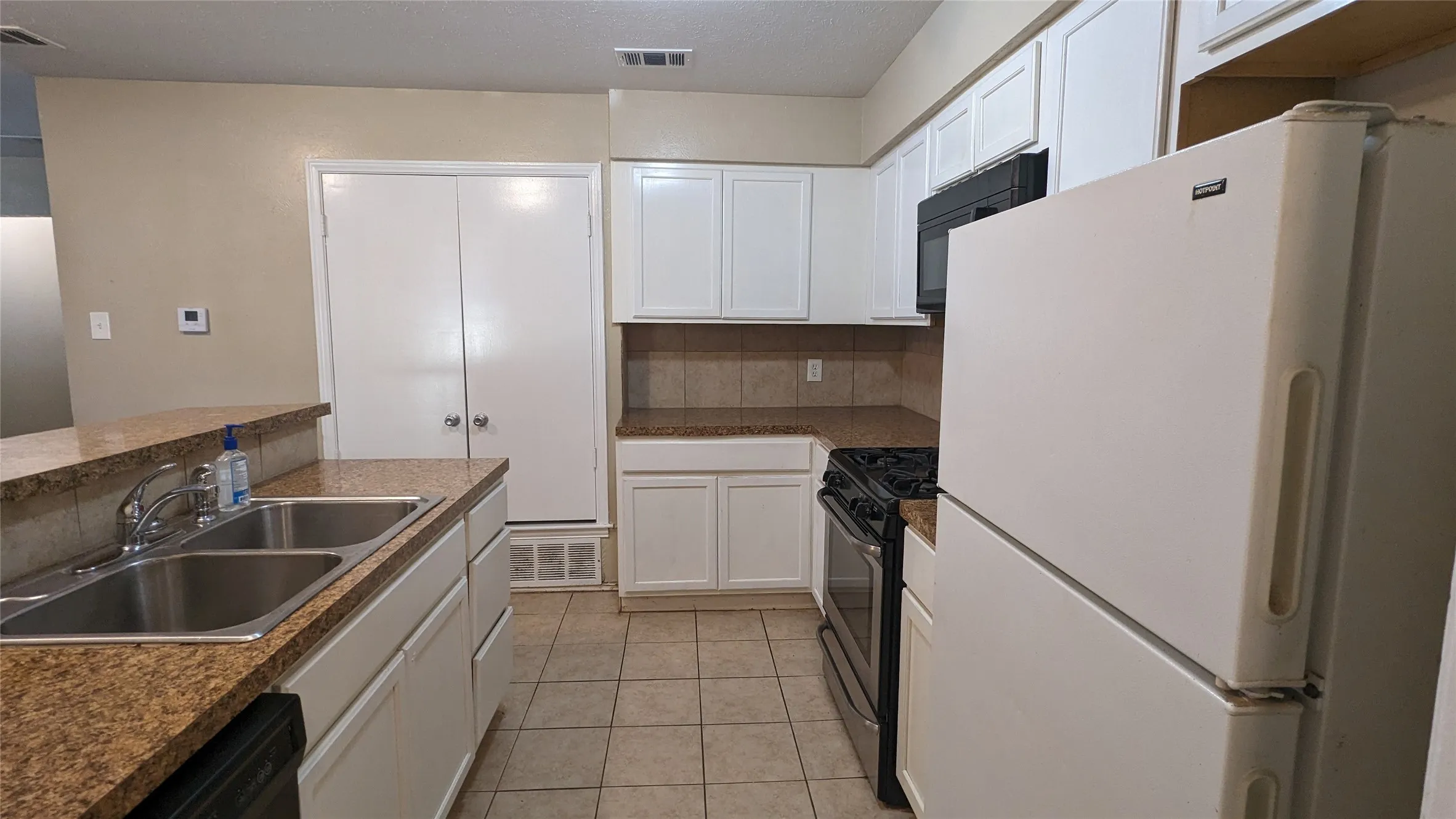 Galley-style kitchen featuring granite-look countertops, white cabinetry, a double stainless steel sink, and tile flooring