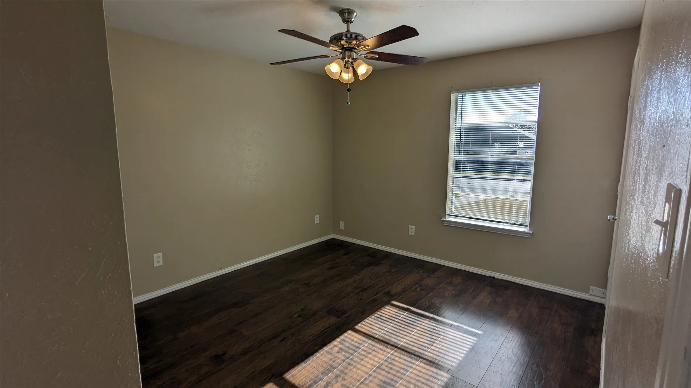 Spacious room featuring rich wood-finish flooring, neutral wall tones, and white baseboards