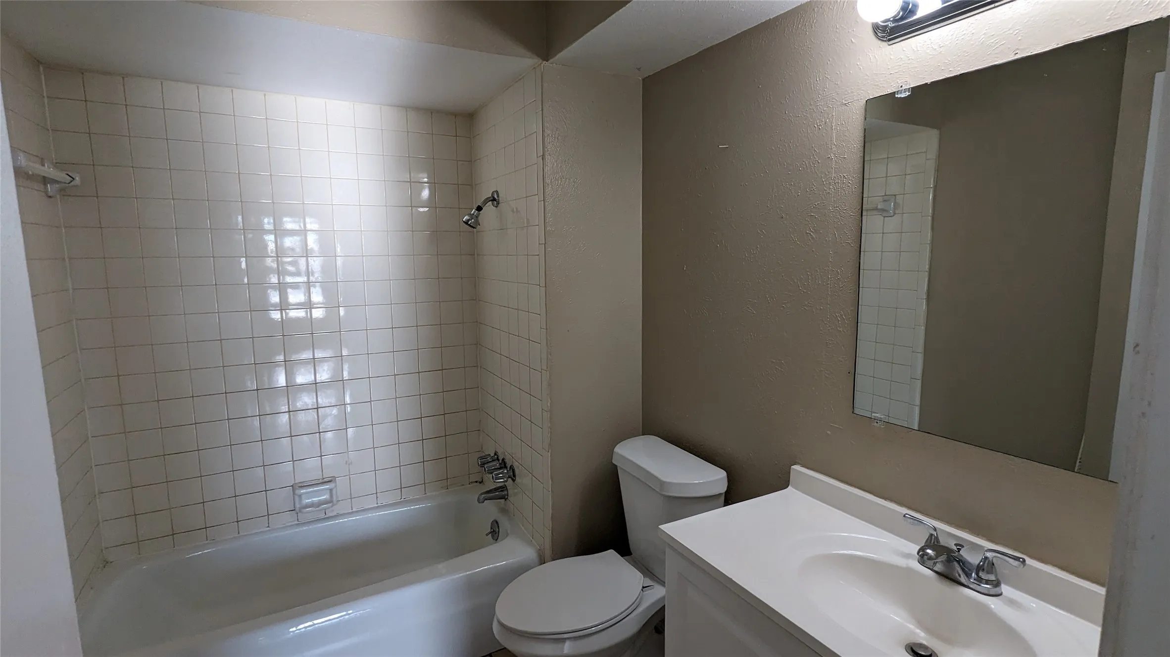 Bathroom featuring a white bathtub, ceramic tile shower surround, a white toilet, and a vanity with an integrated sink