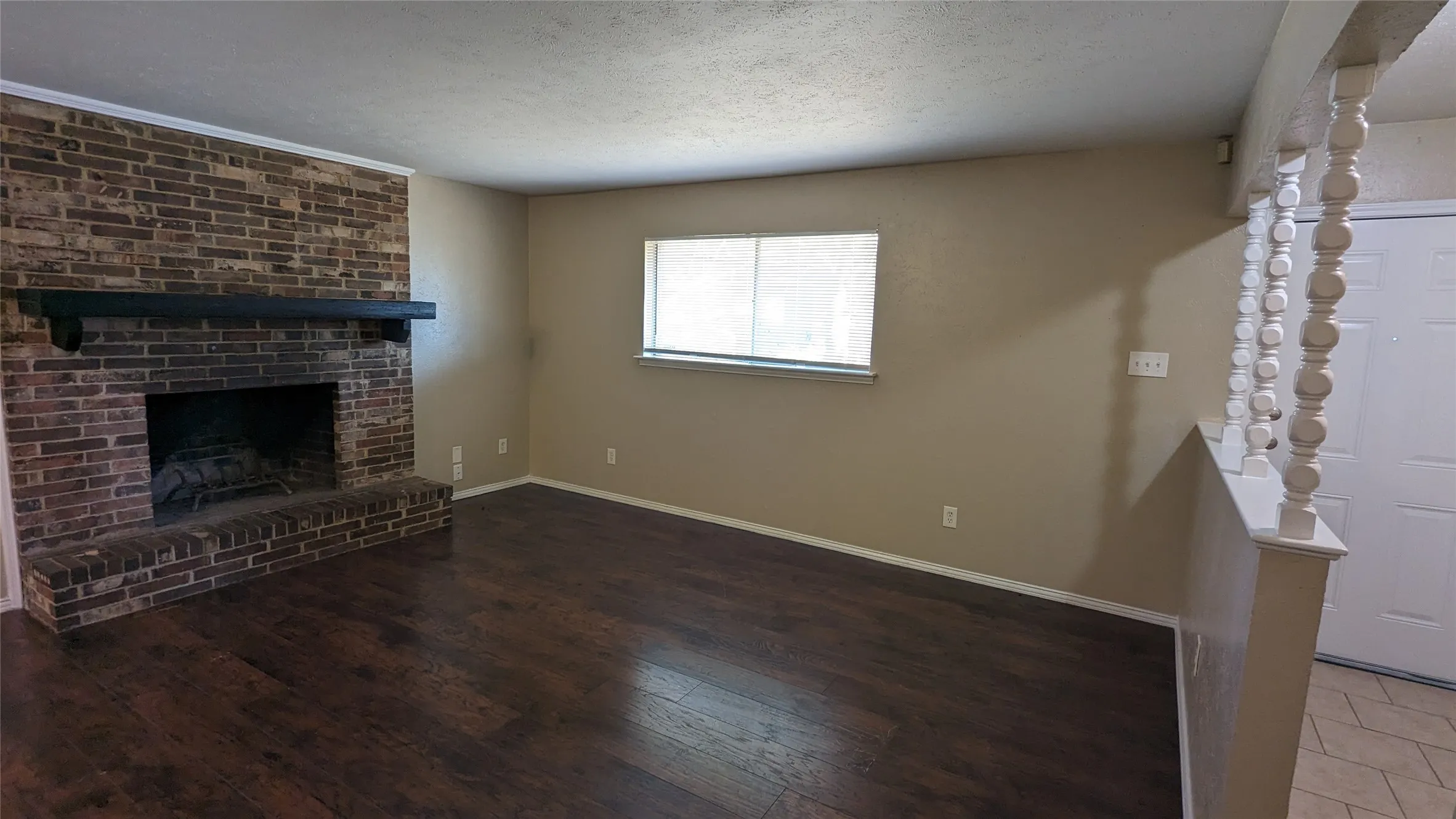 Spacious living area featuring a brick fireplace with a dark mantel, wood-finish flooring, and neutral wall tones