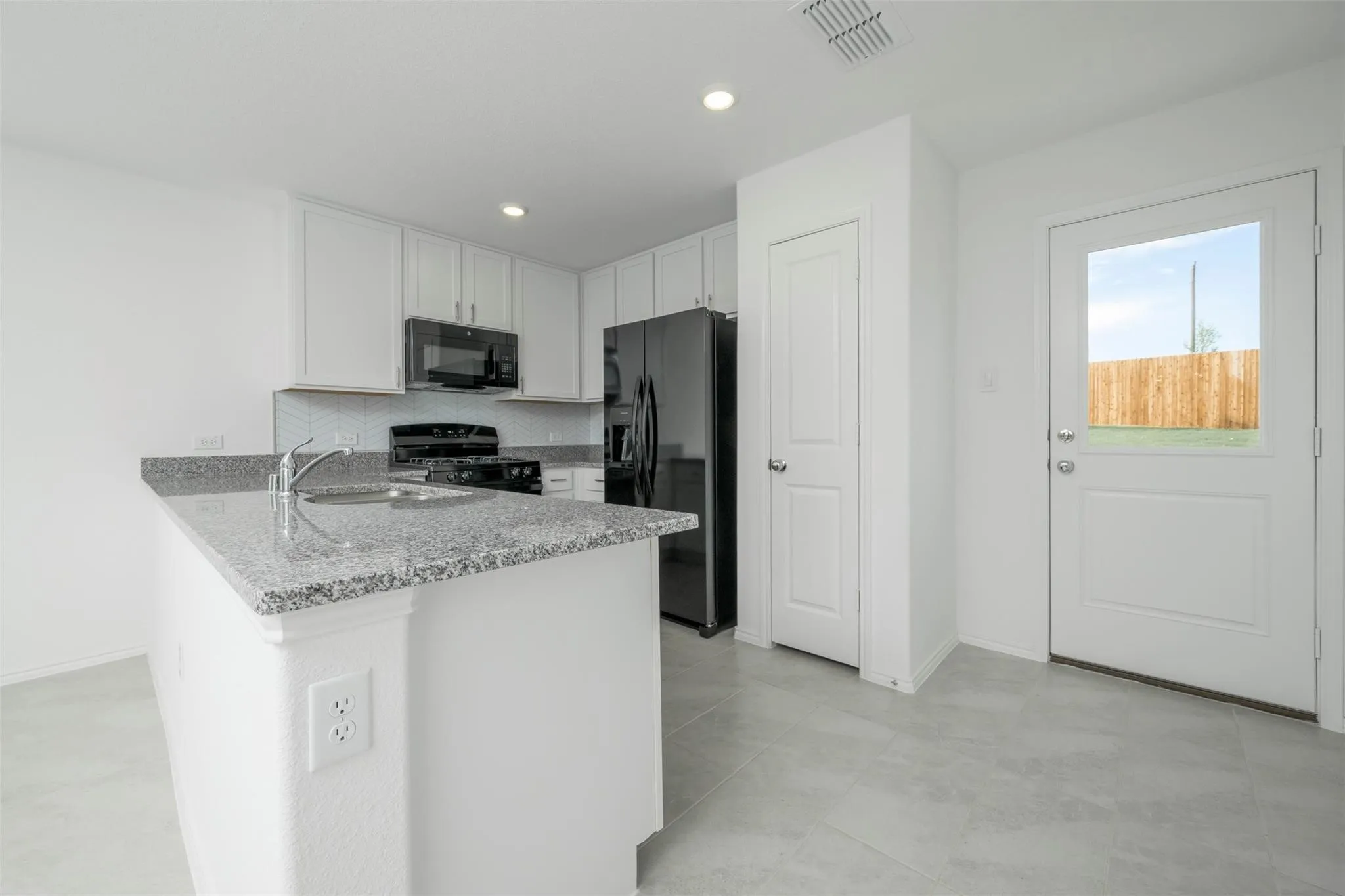 Kitchen featuring white cabinetry, black appliances, light stone counters, backsplash, and light tile floors