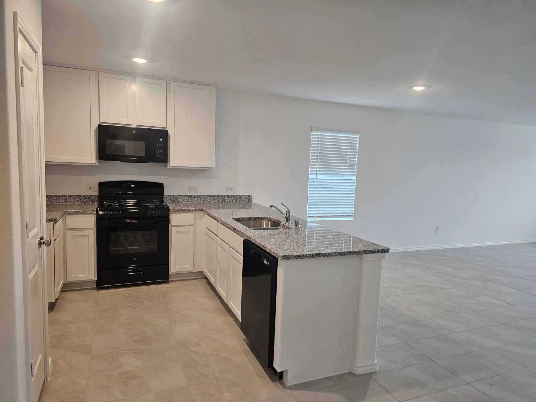 Kitchen with black appliances, sink, light tile flooring, and kitchen peninsula